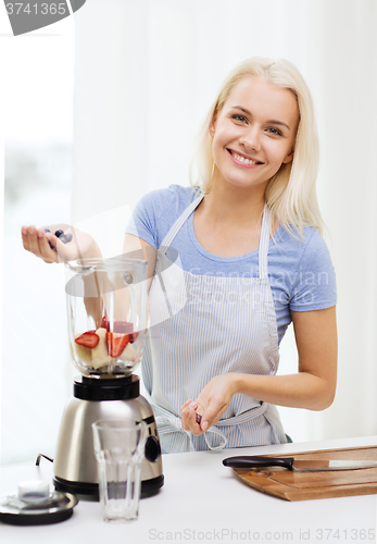 Image of smiling woman with blender preparing shake at home