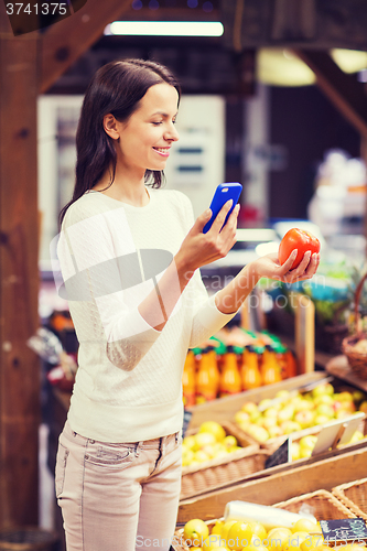 Image of happy woman with smartphone and tomato in market