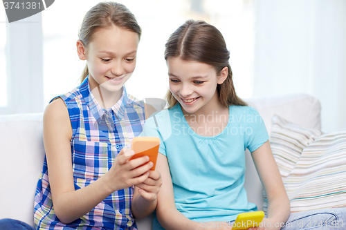 Image of happy girls with smartphones sitting on sofa