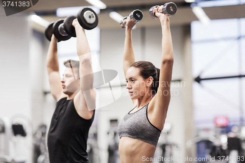 Image of smiling man and woman with dumbbells in gym