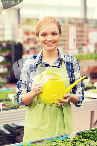 Image of happy woman with watering can in greenhouse