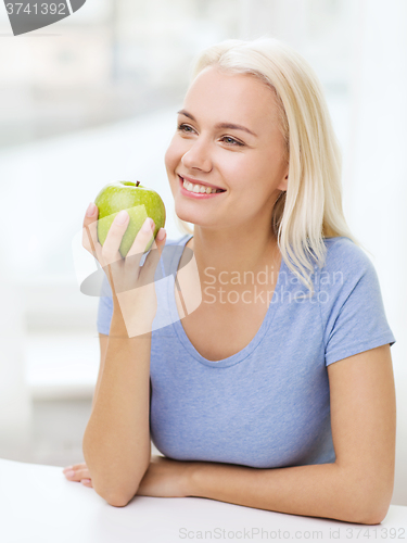 Image of happy woman eating green apple at home