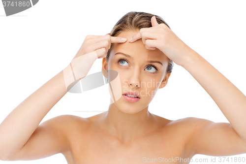 Image of young woman squeezing pimple on her face