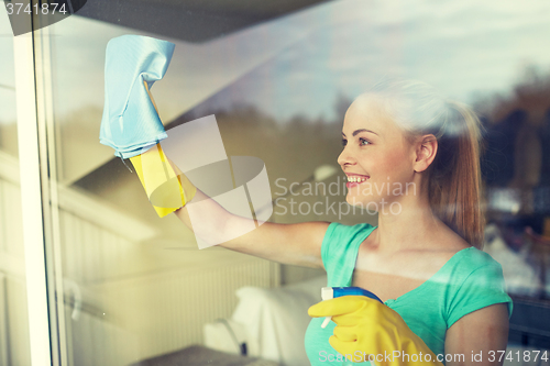 Image of happy woman in gloves cleaning window with rag