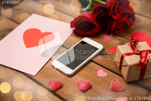 Image of close up of smartphone, gift, red roses and hearts