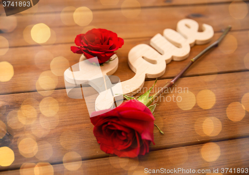 Image of close up of word love cutout with red rose on wood