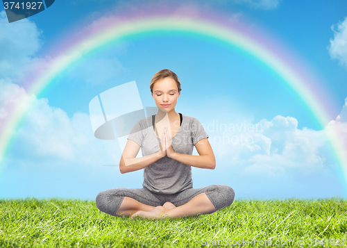 Image of woman meditating in lotus yoga pose over rainbow 