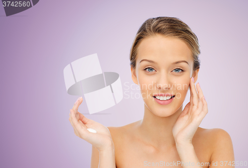 Image of happy young woman applying cream to her face