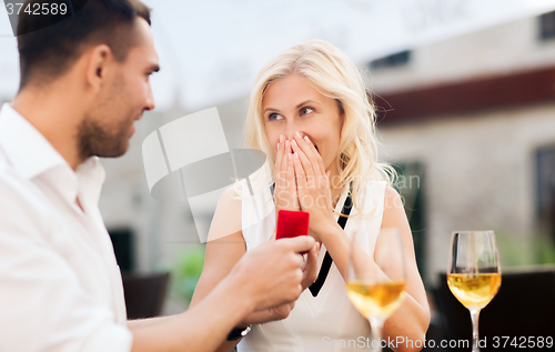 Image of happy couple with engagement ring and wine at cafe