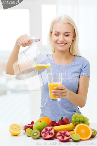 Image of smiling woman pouring fruit juice to glass at home