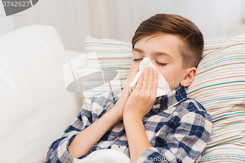 Image of ill boy lying in bed and blowing his nose at home