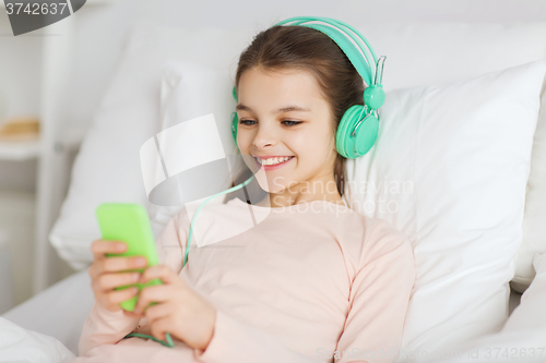 Image of happy girl lying in bed with smartphone at home