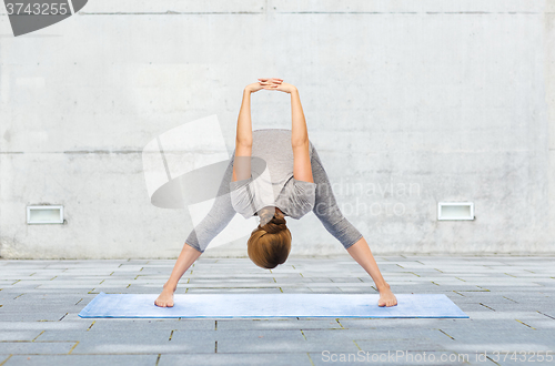 Image of woman making yoga wide-legged forward bend on mat