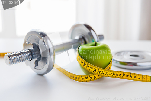 Image of close up of dumbbell and apple with measuring tape