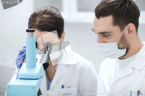 Image of scientists in masks looking to microscope at lab