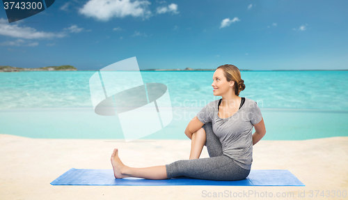 Image of woman making yoga in twist pose on mat over beach 