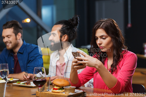 Image of woman with smartphone and friends at restaurant