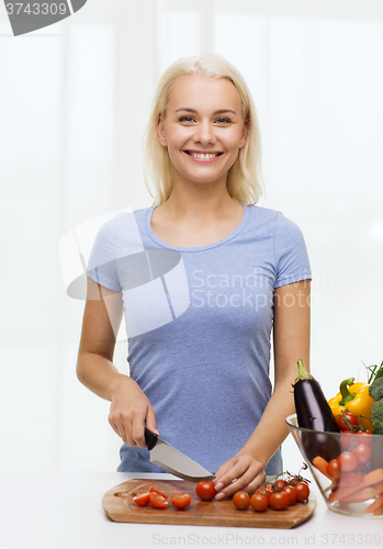 Image of smiling young woman chopping vegetables at home