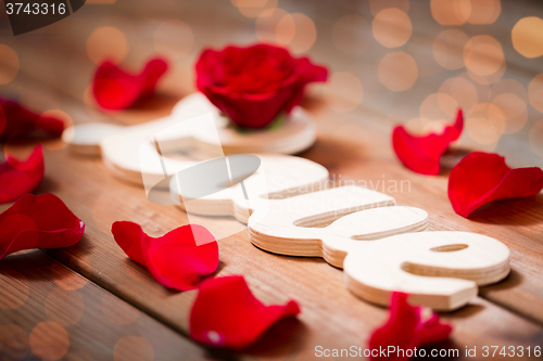 Image of close up of word love cutout with red rose on wood