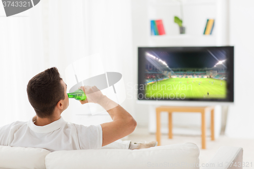 Image of man watching football and drinking beer at home