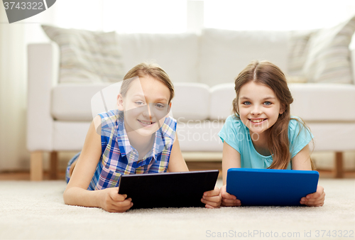 Image of happy girls with tablet pc lying on floor at home