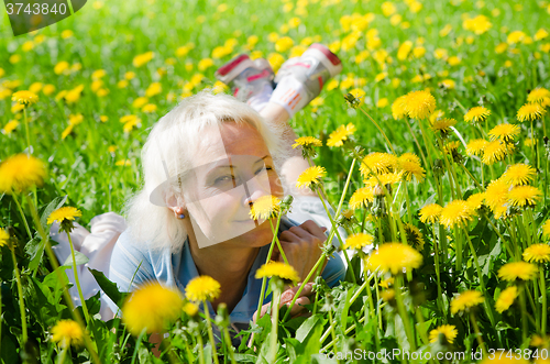 Image of A woman lies in a clearing and sniffs a flower  