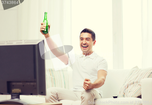 Image of smiling man watching tv and drinking beer at home