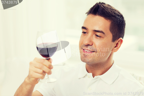 Image of happy man drinking red wine from glass at home