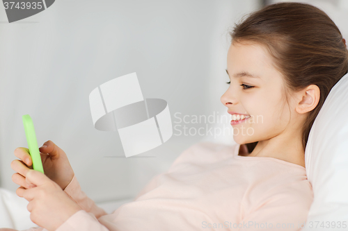 Image of happy girl lying in bed with smartphone at home