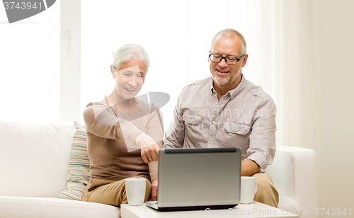 Image of happy senior couple with laptop and cups at home