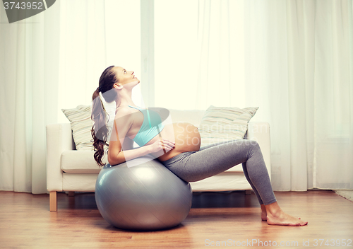 Image of happy pregnant woman exercising on fitball at home