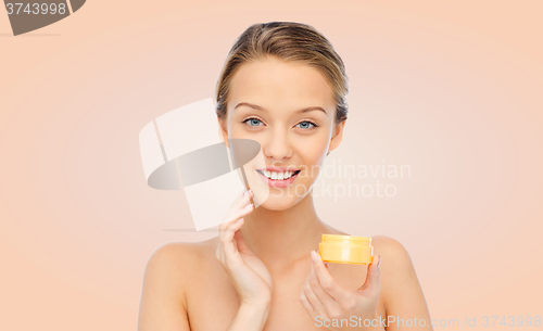 Image of happy young woman applying cream to her face