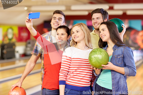Image of happy friends with smartphone in bowling club
