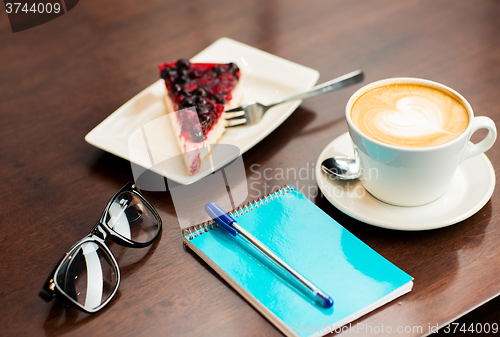 Image of close up of notebook with pen, coffee cup and cake