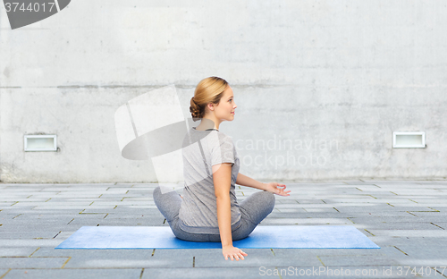 Image of woman making yoga in twist pose on mat outdoors