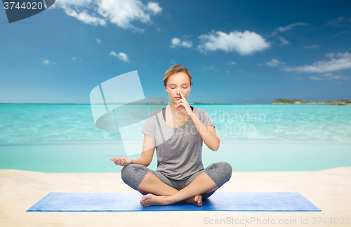 Image of woman meditating in lotus yoga pose on beach
