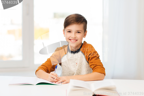 Image of smiling student boy writing to notebook at home