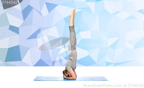 Image of woman making yoga in headstand pose on mat