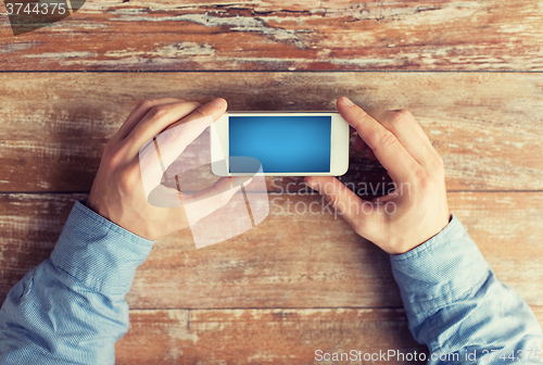Image of close up of male hands with smartphone on table