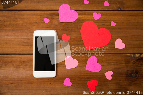 Image of close up of smartphone and hearts on wood