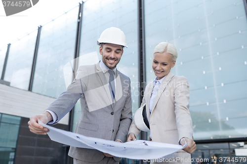 Image of smiling businessmen with blueprint and helmets