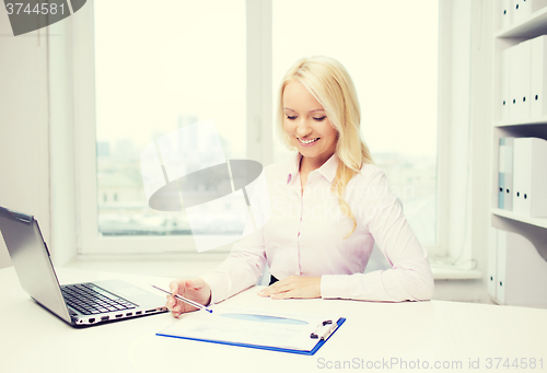 Image of smiling businesswoman reading papers in office