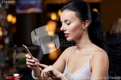 Image of young woman with smartphone at night club or bar