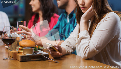 Image of woman with smartphone and friends at restaurant
