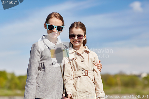 Image of happy girls with smartphone selfie stick