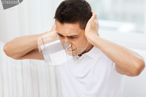 Image of unhappy man closing his ears by hands at home