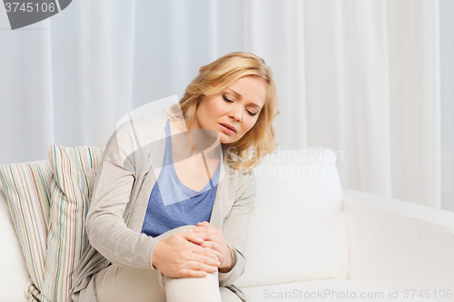 Image of unhappy woman suffering from pain in leg at home