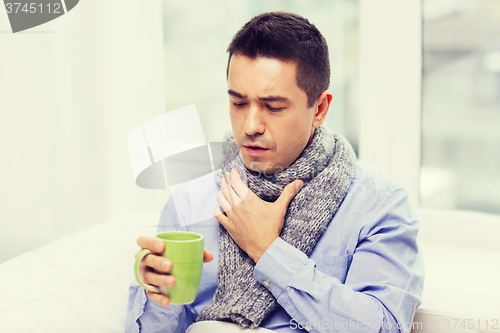 Image of ill man with flu drinking tea and coughing at home