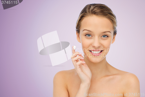 Image of happy young woman applying cream to her face