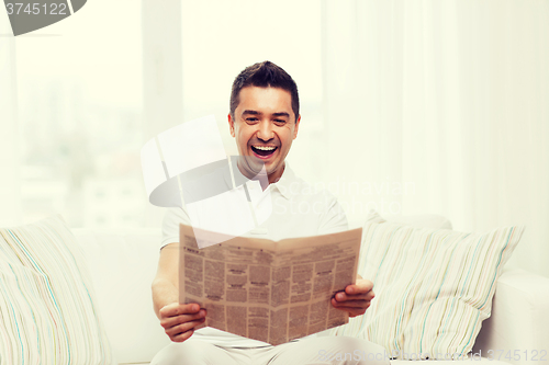 Image of happy man reading newspaper and laughing at home